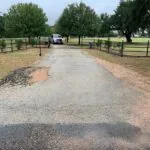 damaged ranch driveway with potholes and uneven asphalt surface