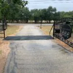 ranch driveway entrance with gate and deteriorating pavement
