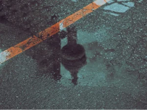 Wet asphalt surface with pooling water near pavement striping and drainage feature