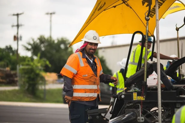 man with hard hat in orange vest on top of fresh concrete
