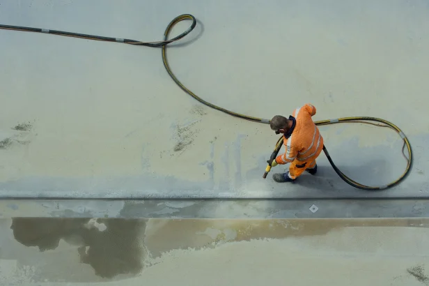Man in orange workclothes sandblasting concrete surface with airpressure hose. Photographed from above.